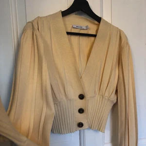 Gul kofta NAKD - Trendig söt ljusgul kofta med bruna knappar från NAKD i storlek Medium. Knappt använd så därmed i fint skick. Tight passform kring midja och handleder. Köparen står för frakt! 