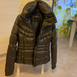 Lindex, XS - Oanvänd. Mycket fin jacka. Varm. Hög krage/halsringning. Två fodrade sidfickor som stängs med metallknapp. En innerficka med en ziplås. Felfri. Halskrage kan justeras på baksida. Hel blixtlås. Mörk grön-svartaktig färg. Maskintvätt i högst 40˚C. 