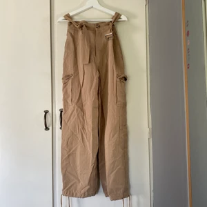 Beige cargobyxor - Beiga Cargo byxor från Zara. Du kan bestämma själv om de ska vara raka eller tighta eftersom man kan knyta så det passar dig längst ner på byxorna. Många fickor och är snyggt till en festival! Köparen står för frakten!