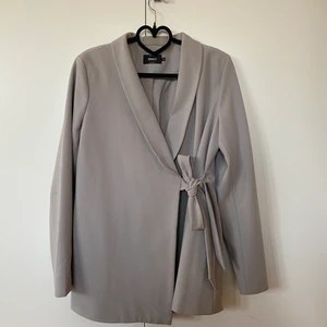 Ljusgrå kavaj med knyte  - Superfin ljusgrå kavaj/blazer som man kan knyta hur man vill i midjan. Den är stretchig och bekväm, med en fin feminin passform. Bilderna gör den verkligen inte rättvisa. Från Only i storlek 36, men köpt på Bubbleroom. Toppenkvalitet och knappt använd. 