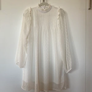 Oanvänd vit klänning/studentklänning  - Supersöt vit och sval klänning som är helt oanvänd. Köptes för att ha till student, men också fin att ha bara under sommaren. Klänningen går till ovanför knäna, har vita meshprickar och söta volangdetaljer. Storlek 36. NLY Trend. 