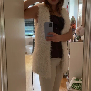 Pälsväst - Vit fluffig pälsväst, har brunt lädersnöre och krokar för att stänga på framsidan. Mycket bra kvalitet.