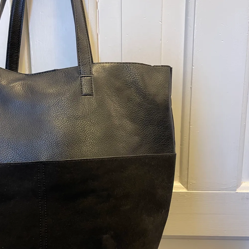 En svart rymlig väska som är i fakeskinn & fakemocka material. Den är köpt på Åhlens för några år sedan. Sparsamt använd och i bra skick!. Väskor.