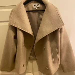 Beige kort kappa  - Kappa från Na-kd, ny kostar 899kr, jag säljer för 700kr ink frakt. Använd 2-3ggr. Storlek 36!            Bud just nu: 870kr varan är helt slutsåld i alla storlekar på hemsidan!! 