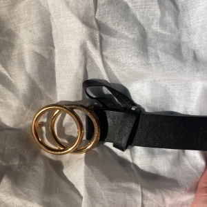 RING SKÄRP - Säljer mu detta fina klassiska skärp med två ihopsatta guldiga ringar vid fronten! Skärpet är hyfsat använt och har inte märkvärdigt mycket slit. Som ni ser på den första bilden har de guldiga fått lite brons färg på vissa ställen men inget allvarligt! Skärpet har extra många hål som jag stämplat själv! Skriv gärna för frågor eller bildar osv! ❤️ Skulle gissa att den är köpt ifrån HM, KAPPAHL eller Lindex! 