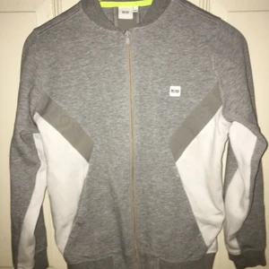 Grå Hugo Boss set FINT skick 14/S  - Grått/vitt mjukisar med kofta + byxa från Hugo Boss i  mycket fint skick. Muddar längst ned på jackan men rakt avslut på byxorna, Neongula detaljer. Storlek 14/S