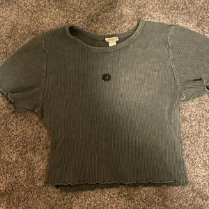 Croppad t-shirt - grön croptop med en sol på. använt 2 gånger, det är jätte bra material och den sitter jätte skönt, den är i strl S men den är stretchig så den skulle kunna passa M också:)