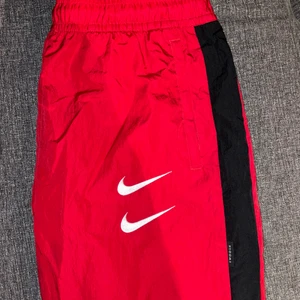 Nike track pants stl.M - Röda Nike träningsbyxor i ett vindtätt material. Storlek M, jag är 180 cm lång och bär vanligtvis M/L. Sparsamt använda och därför inga slitningar eller liknande. Köpta för 649:- på NLYMAN i september 2020. Köparen står för frakt. Skriv till mig vid frågor/fler bilder