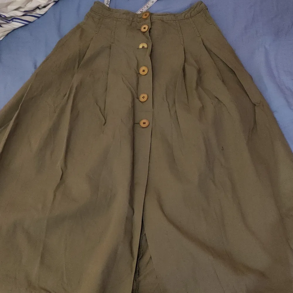 En lång grön kjol med knäppning fram. Midjan är 36 cm och längden är 80 cm.. Kjolar.