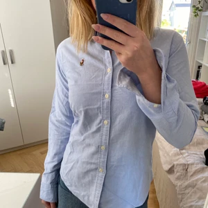 Blå skjorta från Ralph Lauren - Säljer denna ljusblåa skjorta från Ralph Lauren i storlek 4 (vilket typ motsvarar 34/36). Den har en liten fläck på sig vid högra nyckelbenet (se bild två). Annars är den i gott skick.  En fraktkostnad tillkommer om inte annat är överenskommet.