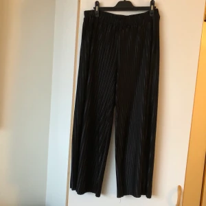 Svarta byxor från MQ i storlek M - Festliga ribbade byxor från MQ i storlek M! De har en lös passform och är croppade vid anklarna. Supersköna och sparsamt använda.