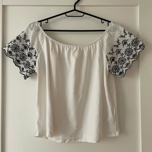 Vit blus med svarta broderier - En fin vit off shoulder topp/blus i strl XS, passar även S! Ärmarna har svarta broderier 💖 Tröjan är i gott skick!