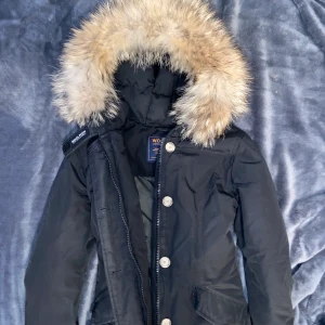 Svart Woolrich jacka  - Svart Woolrich jacka med fickor och knappar under kedjan, figursydd, mycket bra skick. Passar folk med xs/s. Använd mindre än 6 månader. Priset kan diskuteras i privat, skriv för fler bilder eller frågor💞