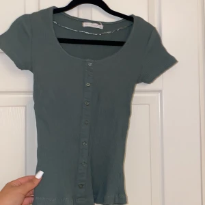 Militär grön T-shirt  - Ser mer militärgrön ut i verkligheten, har knappar som inte går att öppna, endast för detaljer, ribbad.
