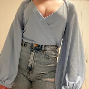 Ljusblå tröja med ballongärmar  - Superfin askungen-inspererad omlotttröja i ljusblå färg med ballongärmar. Perfekt att ha vid finare tillfällen med ett par kostymbyxor eller när man känner för att göra ens outfit lite mer fancy! Den är i storlek XS men är superstrechig så den är snarare S-M 💙