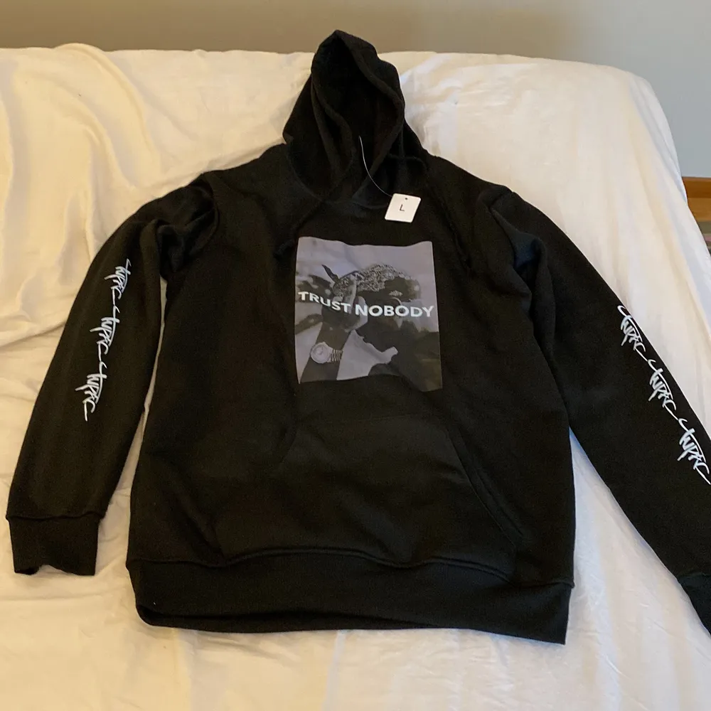 En svart tupac hoodie med en luva, en ficka i mitten, och det står tupac på armarna. Den är lite för tajt för L men skulle passa perfekt för M. Det är bara att höra av sig med frågor eller intressen vid köp. . Hoodies.