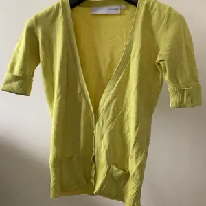 En väldigt fin överdel som både kan använda som t-shirt och kofta i en fin gul/grön färg, men knappar och fickor och djup v-ringning