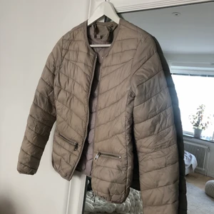 Tunn beige dunjacka Amisu strl. 36 - Tunn beige dunjacka Amisu strl. 36. Fraktkostnad ingår ej i priset. 
