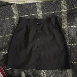 Svart kjol - Svart kjol med knappar och fakefickor. Gissar storlek M