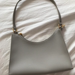 Grå väska - Grå väska med gulddetaljer ifrån SHEIN, aldrig använd. Har ett fack i. Skickas eller mötas upp i Kalmar. Tar Swish 