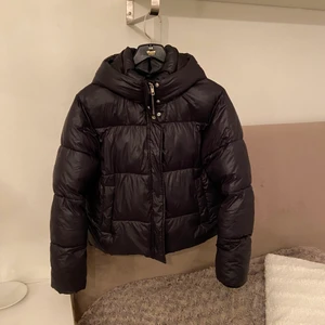 NLY TREND puffjacka svart strl 38 - Puffjacka från NLY TREND i svart, inga slitage köpt 2020. Dragkedja och knappar fram hela vägen upp i kragen, två fickor fram utsida, en liten ficka på insida. Luva. Original pris 699kr (Frakt exklusive pris)