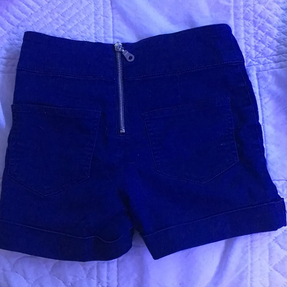 Detta är ett par shorts. Dom är marinblå med silver knappar på, har även en dragkedja i bak.. Shorts.