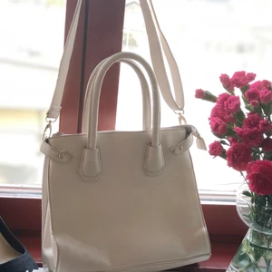 krämvit väska  - medelstor krämvit väska med olika fack och två fickor med dragkedja! (finns ett litet svart märke på baksidan) Leverans: kunden står för kostnaden