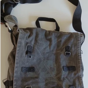 Väska med döskalle motiv  - Intressekoll på en väska jag köpt från tradera. Grå axelremsväska i tyg med 3 fack och dödskallemotiv på locket på framsidan. Den är i bra skick och rymmer mycket<33. Det är bara att skriva för fler bilder eller frågor☺️