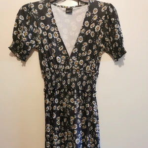 Blommig klänning  - V-ringad klänning med fina tusenskönor/daisy's från Gina Tricot. Lite tungt tyg, så faller fint. Puffärm och lite bredare resor/smock i midja och ärmslut. Använd ett fåtal gånger, i bra skick. (Lägger all frakt på spårbart, men går ev att få billigare med porto) 