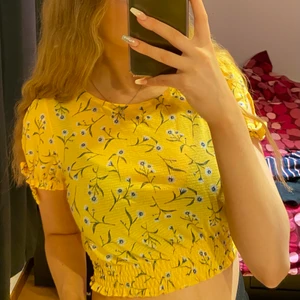 Gul sommerblus med blommor - Gul sommerblus med blommor. Man kan själv knyta den på armen. Använt fåtal gånger, den är i väldigt fint skick. 