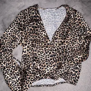 En leopard blus/skjorta i storlek 36 ifrån NA-KD. Använd 1 gång och därav i bra skick. Materialt är som silke med ett resårband runt midjan och uppknäppbar vid brösten och i armarna. 