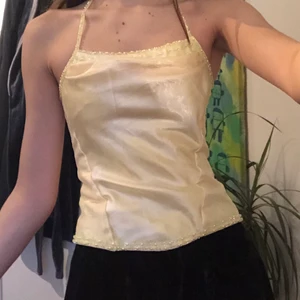 Gul korsett-topp - Halter-linne i korsett stil gjord i glansigt silkes-aktigt gult tyg. Finns tyvärr ingen lapp i den så vet inte exakt material eller storlek. Köpt på humana men knappt använd av mig då tyvärr jag har för breda axlar för den. Den är i mycket bra skick och de lodräta sömmarna är förstärkta med plastpinnar (?) som brukar finnas i korsetter. Dessutom finns det små pärlor vid alla kanter