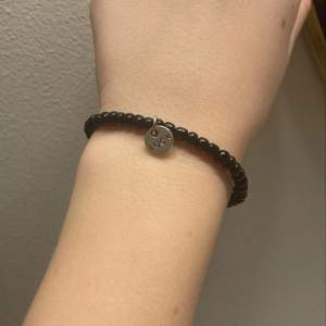 Detta är ett svart armband med en berlock där de står ”luck”