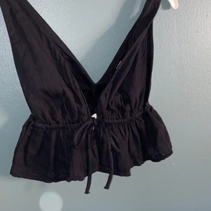 Bikbok svart mini topp med volang⚡️ - Kort topp i mjuk, ekologisk bomull med breda axelband och djup urringning fram och bak. Toppen har snörning under bysten som knyts framtill, och bred volangkant nedtill. Toppen är endast använd vid provning. Storlek S. Högsta budet vinner✨Köparen står för frakten ( frakten kostar 45).