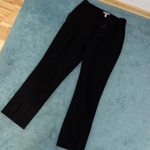 Svarta kostymbyxor med slit - Högmidjade svarta kostymbyxor med slits framtill nertill. Storlek: 36. Toppskick