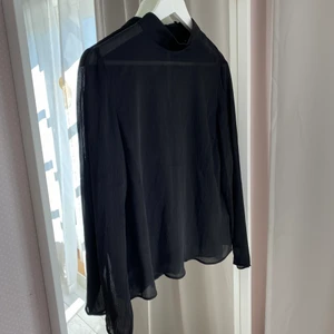 Svart blus - Svart blus med halvgenomskinligt material som är lite randigt. Superskön med två knappar i nacken att stänga med. 