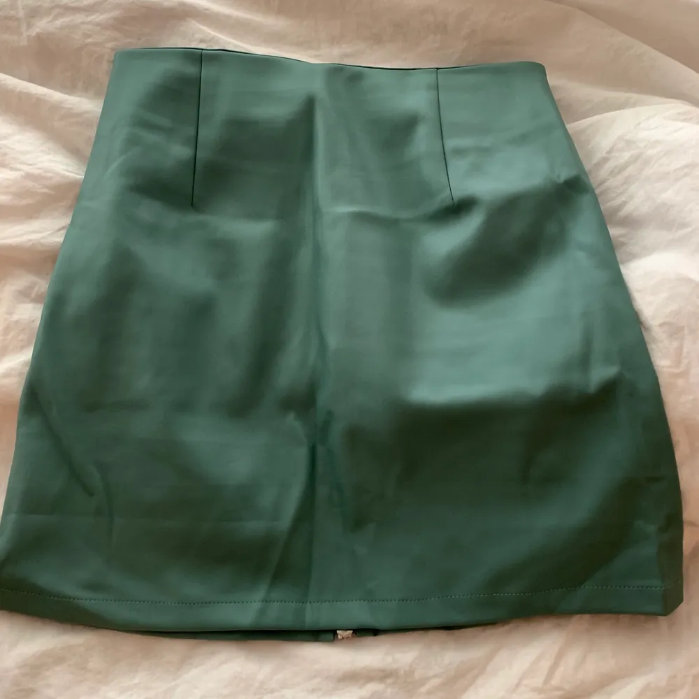 En kjol i skinn imitation med en fräsch grön/blå färg. Kjolen har en dragkedja där fram som går att öppna upp helt. . Kjolar.