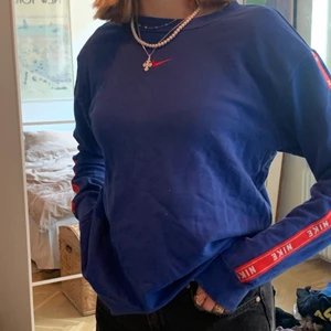 Snygg sweatshirt från Nike - Säljer denna skitsnygga sweatshirten från Nike. Jättefin blå färg med röda stripes med Nikeloggan på båda ärmarna. Storlek XS men passar S också. Sparsamt använd så i fint skick. Den har en jättesnygg fit och är lagom lång. Säljer för 150kr.