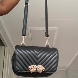 Svart väska  - Svart axelväska med guld lejon detalj 