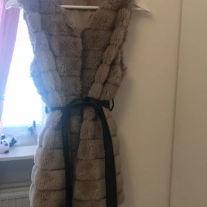 FEJKPÄLS VÄST - Väst i fejk päls, beige färg, tillhörande avtagbart bälte i fejk skinn. 