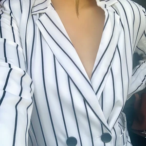 Blazerklänning - Urringad vit blazerklänning med svarta ränder. Väldigt urringad. Är i storlek M köpt från nasty gal.