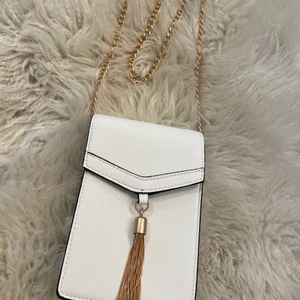 Oanvänd Vit väska - Oanvänd, vit rektangulär väska med en söt guldtoffs. Mocka på insidan och läderakyigt material på utsidan Passar till alla tillfällen, och unik form. Pris kan diskuteras vid snabb affär