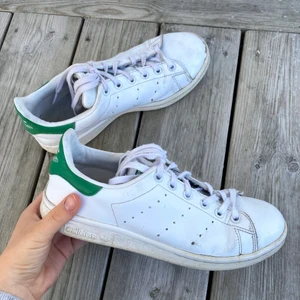Stan Smith Skor Vit/Grön - Vita stan smith sneakers från adidas. Finns några slitningar på men i övrigt bra skick! Skorna är i storlek 38 2/3 men de är lite små i storleken så de passar perfekt om man har storlek 38☺️