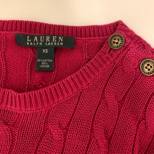 Stickad Ralph Lauren tröja - Otroligt fin och elegant tröja från Ralph Lauren♥️ Garnet är aningen blankt med en vinröd/mörkrosa nyans. På ena axeln sitter mässingfärgade knappar. Tröjan är endast använd 2-3 gånger och är i nyskick🥰