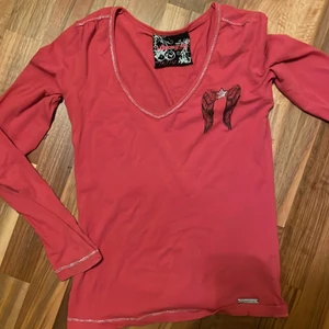 ”y2k-aktig” rosa tröja - Rosa tröja med många små detaljer, b.la. Rhineatones och änglavingar på ryggen. Köpt second hand men har inga defekter. Osäker på storlek, jag är xs/s i överkropp och den passar mig men tror även den skulle passa m då den är stretchigt material❤️‍🔥 Köpare står för frakten❤️‍🔥
