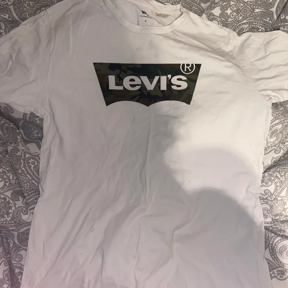 En vit Levis t- shirt med kamouflage tryck i st M. Är använd rätt mycke men har tagit bra hand om den och den är fin i skicket, frakt tillkommer 66kr. T-shirts.