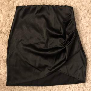 En superfin svart kort sidenkjol från Nelly som har som en liten mini slits samt lite omlott tyg som gör kjolen ännu snyggare! Använd max 3 gånger och säljer för att den är för liten. Köparen står för frakt🖤