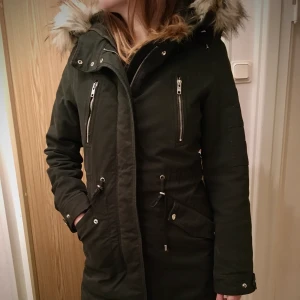 Vinterjacka Bershka mörkgrön - Superfin och varm vinterjacka ifrån Bershka. Bra skick, fantastiskt skönt innerfoder som även är avtagbart vid behov. Fluffig och mysig stor luva där även pälsen (fusk) är avtagbar. Färgen är fin mörkgrön och drar lite mot svart. Normal i storleken. Säljer pga att den blivit för liten för mig. 