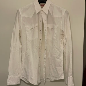 Vit Levi’s skjorta - Vit Levi’s skjorta med tryckknappar. Lite i western stil med fickorna och över axlarna. Tunn och skön för sommarn och gör sig väldigt bra till jeans. Frakt tillkommer