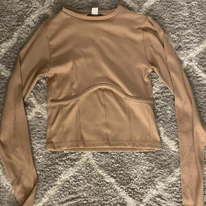 Ribbad långärmad tröja - En superfin ribbad tröja i beige/rosa som har en en bygel under vardera bröst. Knappt använd men säljer för att den tyvärr är för liten för mig. Passar dig som bär S/XS💜💜